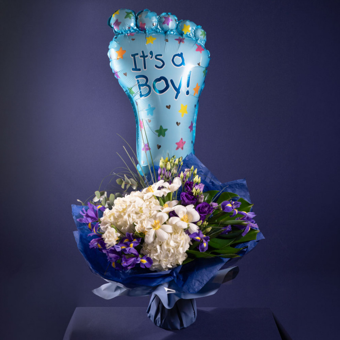 Perspectiva cu florile din Buchet de flori pentru nou-nascut "It's a Boy", varianta Standard, compusa din 2 hortensii albe, 3 flori de lisianthus mov, 5 fire de beargrass, 4 crengute de eucalipt, 9 irisi, 2 frunze de monstera, 2 frezii albe, 5 lalele albe si 1 balon picior.