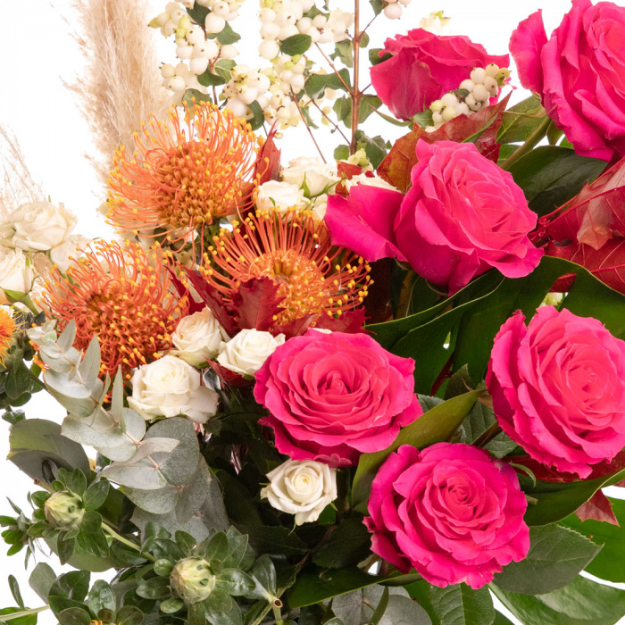 Detaliu de aproape cu florile din Buchet de toamna exotic, varianta Deluxe, compus din 2 frunze de monstera, 2 fire de pampas, 2 crengute de symphoricarpos, 3 flori de leucospermum, 3 flori de carthamus, 6 trandafiri Pink Floyd, 3 trandafiri ramificati albi si 2 crengute de quercus